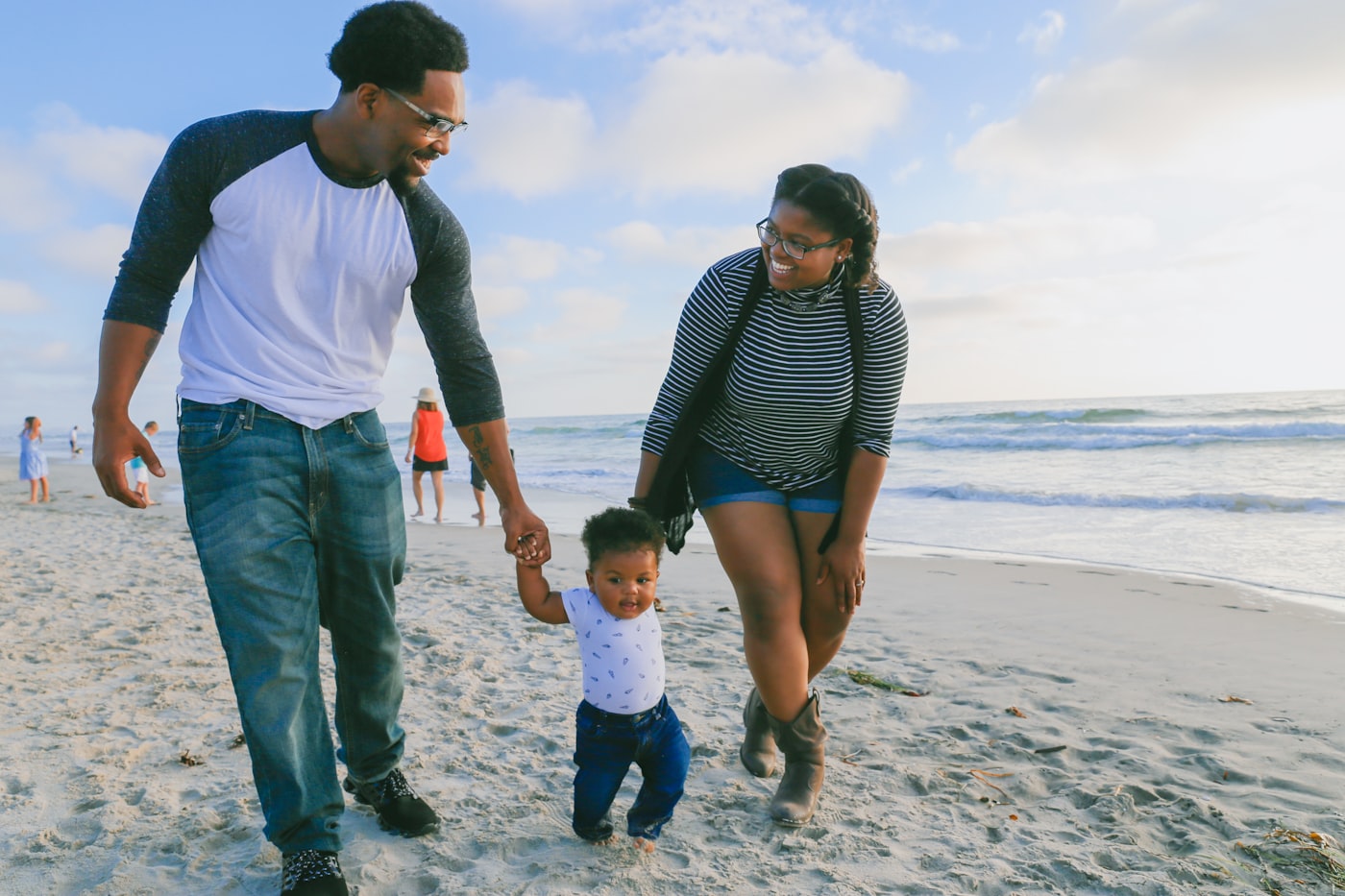 Two parents walking on the beach holding hands with their toddler