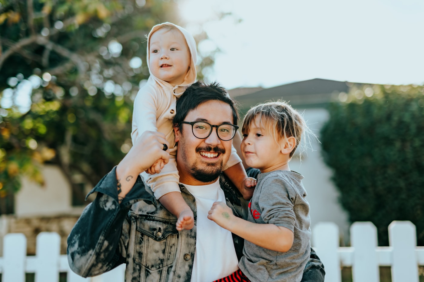 A laughing father carrying his two young children outdoors