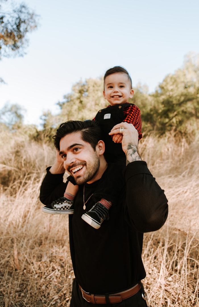 A smiling father carrying his young son on his shoulders